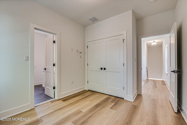 unfurnished bedroom with a closet, baseboards, visible vents, and light wood-style floors