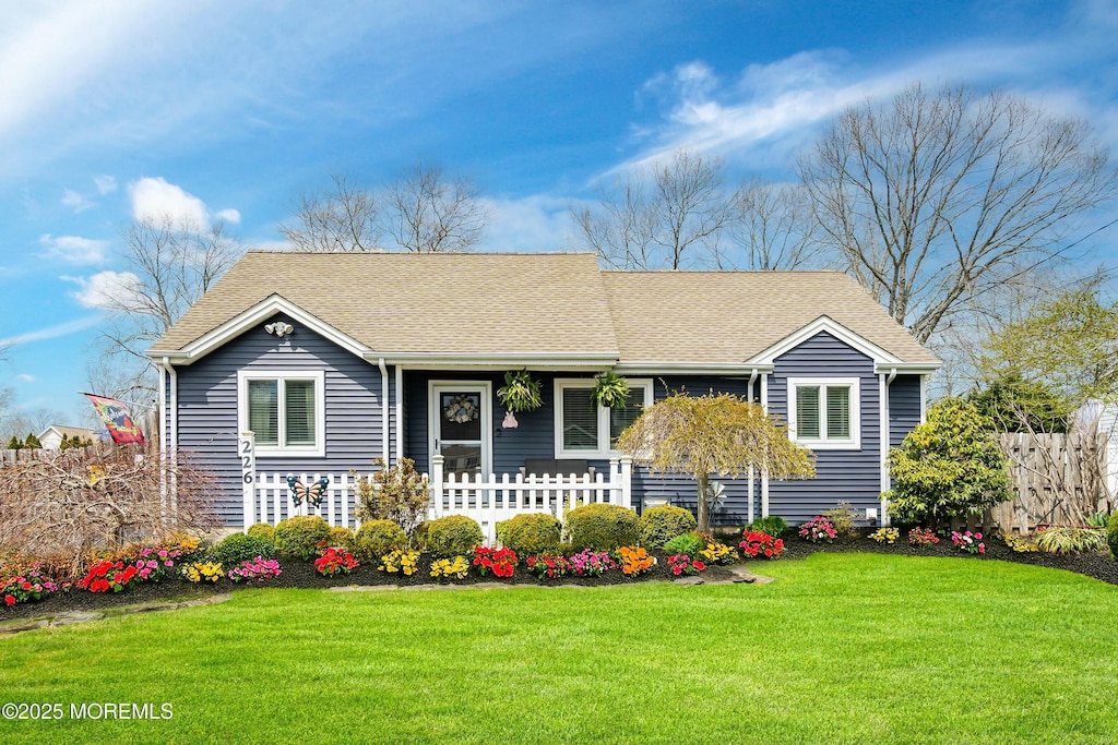 ranch-style home with fence, a shingled roof, and a front lawn