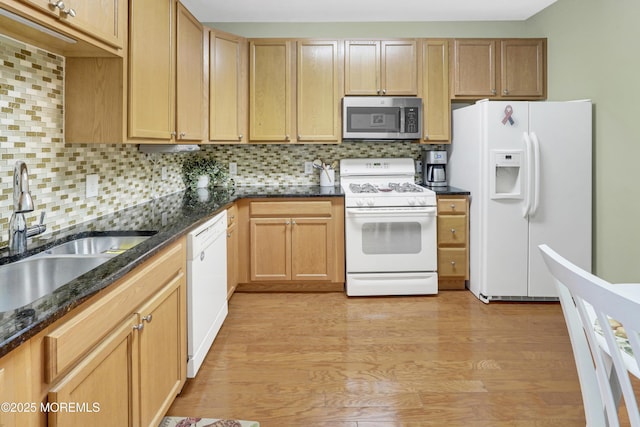 kitchen featuring a sink, white appliances, light wood-style flooring, dark stone counters, and tasteful backsplash