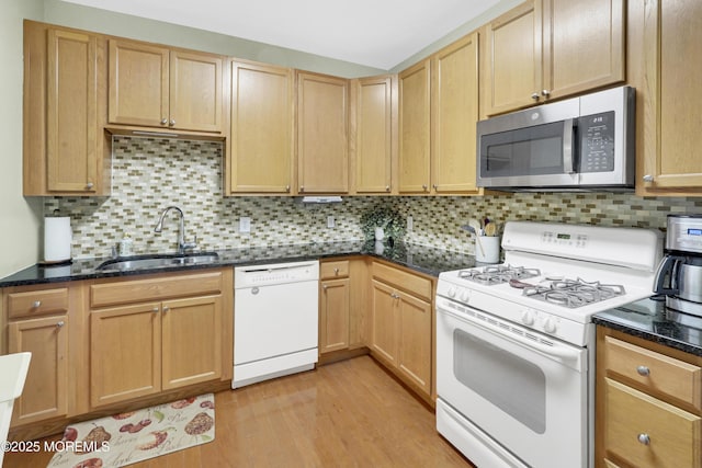 kitchen with a sink, light wood-style floors, white appliances, dark stone counters, and tasteful backsplash