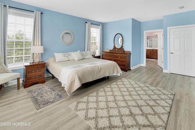 bedroom with baseboards, ensuite bath, and wood finished floors