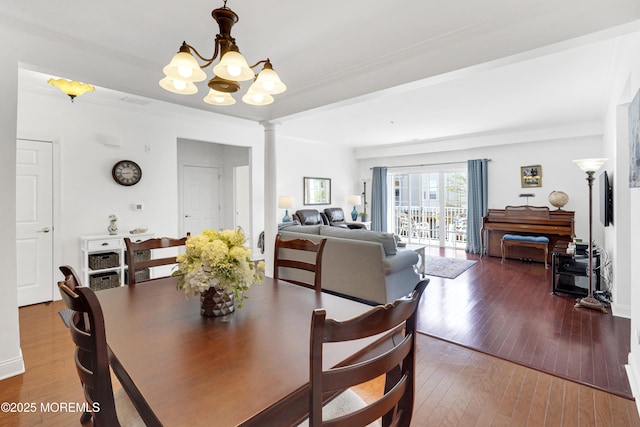 dining area with ornate columns, wood-type flooring, crown molding, and a chandelier