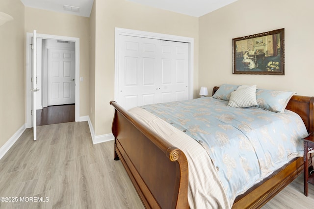 bedroom with baseboards, a closet, light wood finished floors, and visible vents