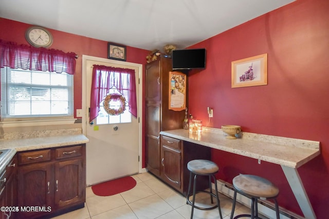 kitchen with a baseboard heating unit, light tile patterned flooring, light countertops, and a breakfast bar