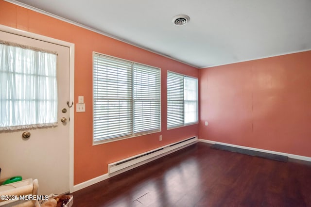 spare room featuring dark wood-type flooring, a healthy amount of sunlight, a baseboard heating unit, and visible vents