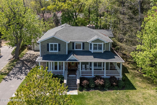 view of front of property featuring covered porch, a chimney, a front lawn, concrete driveway, and a shingled roof