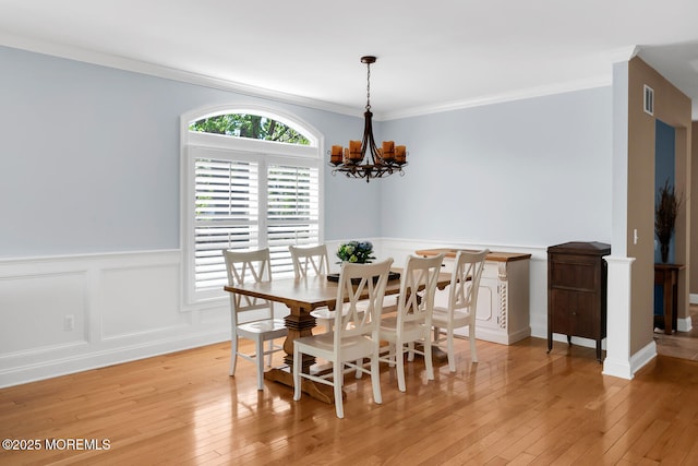 dining room with a decorative wall, an inviting chandelier, a wainscoted wall, and light wood-type flooring