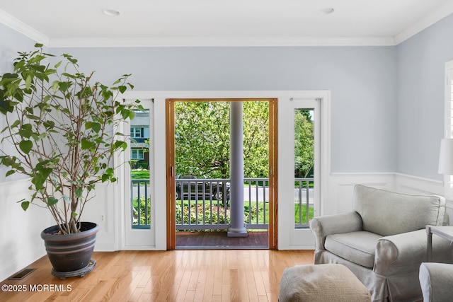 doorway with crown molding, plenty of natural light, light wood finished floors, and visible vents