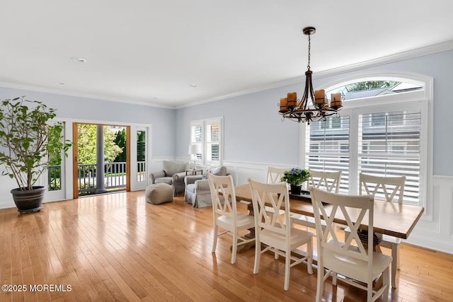 dining room featuring crown molding, wainscoting, light wood-type flooring, an inviting chandelier, and a decorative wall