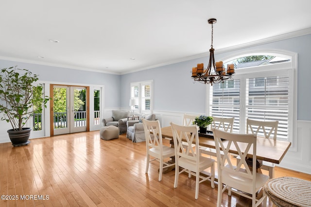 dining space with a wainscoted wall, a chandelier, light wood-style floors, ornamental molding, and a decorative wall