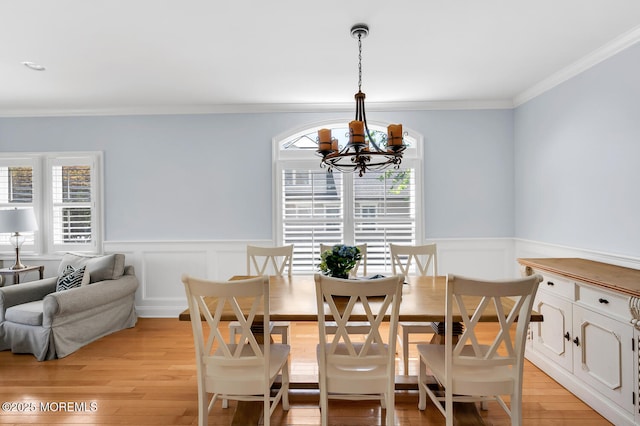 dining area with light wood-style floors, ornamental molding, a wainscoted wall, and a chandelier