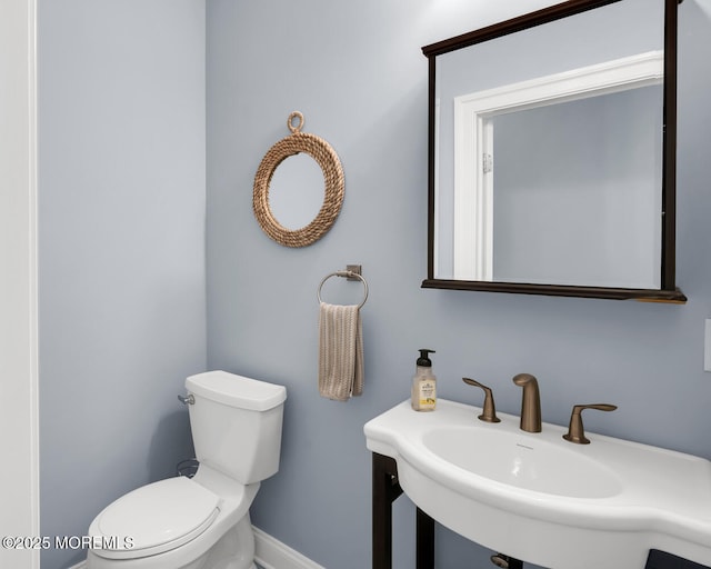 half bathroom with toilet, baseboards, and a sink