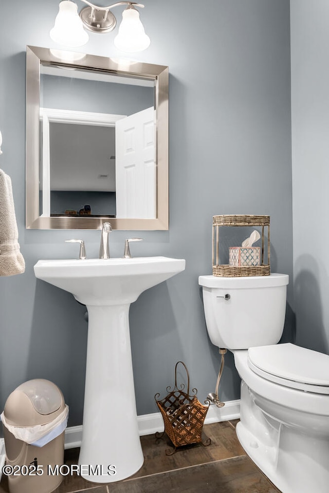 half bath featuring a sink, baseboards, toilet, and wood finished floors