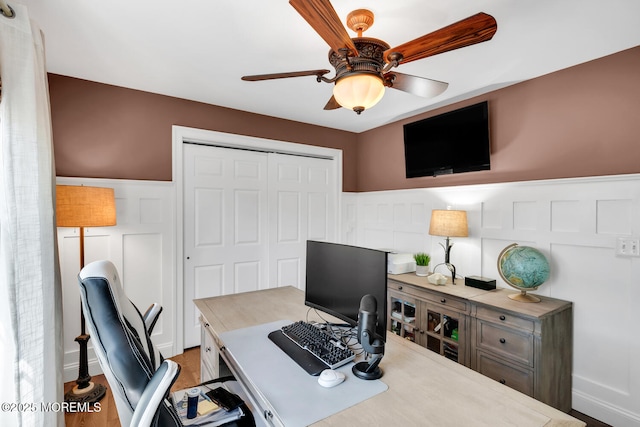 office space with wainscoting, a decorative wall, and a ceiling fan