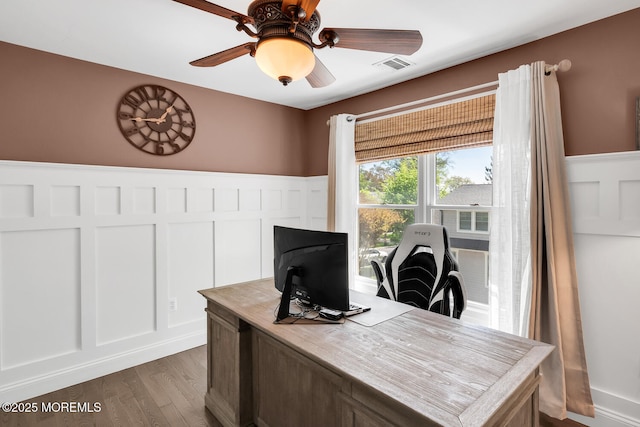 office area featuring ceiling fan, visible vents, wood finished floors, and a wainscoted wall