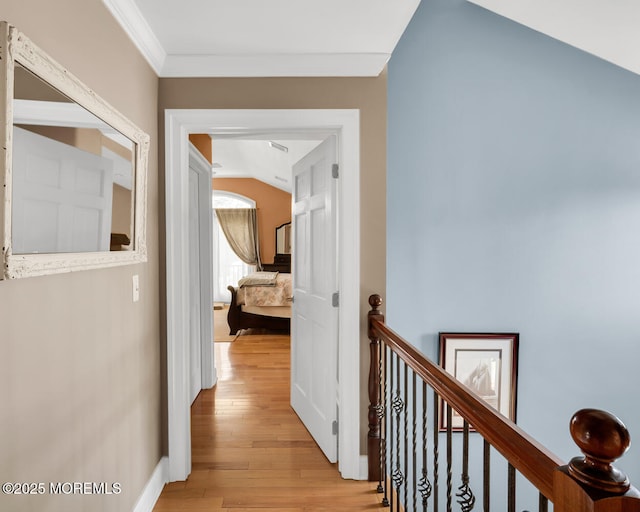 hallway featuring crown molding, lofted ceiling, baseboards, light wood-style flooring, and an upstairs landing