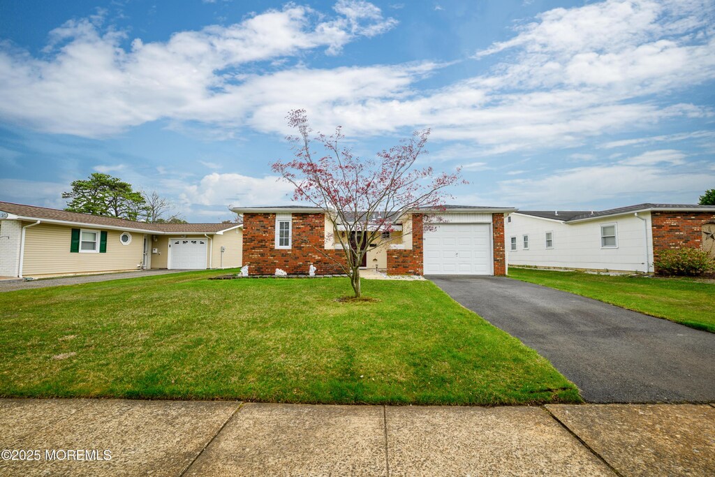 view of front of home featuring an attached garage, a front lawn, aphalt driveway, and brick siding