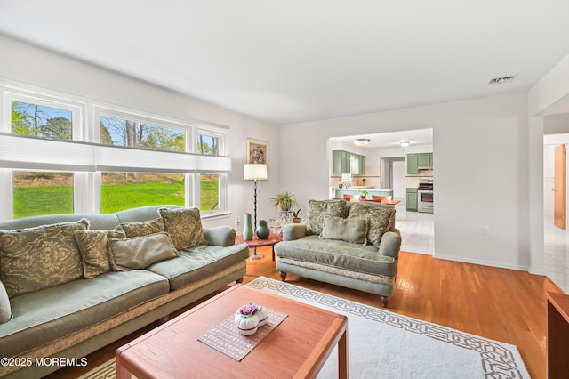 living area featuring light wood-type flooring, visible vents, and baseboards