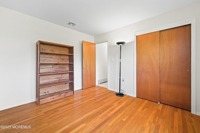 unfurnished bedroom with a baseboard radiator, a closet, light wood finished floors, baseboards, and visible vents