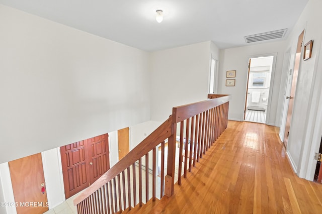 hallway featuring light wood finished floors, visible vents, and an upstairs landing