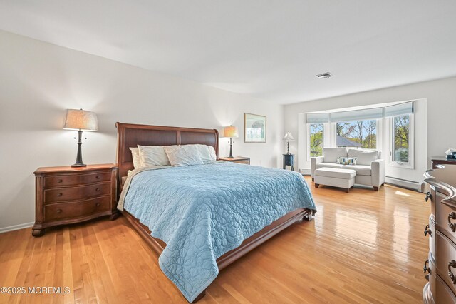 bedroom featuring a baseboard heating unit, visible vents, and light wood finished floors