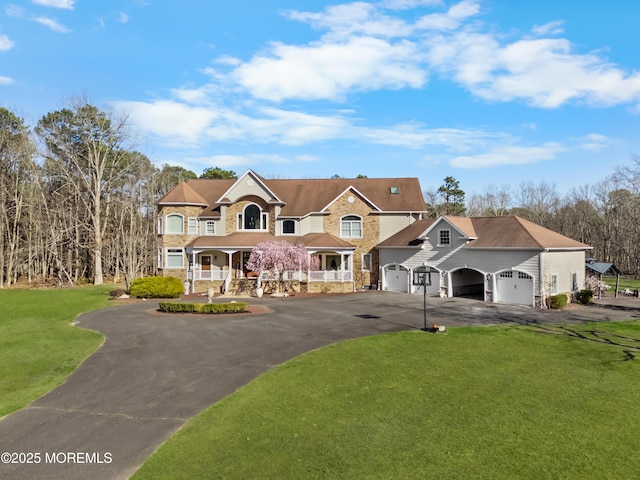 view of front of property featuring driveway, stone siding, a porch, a front yard, and a garage