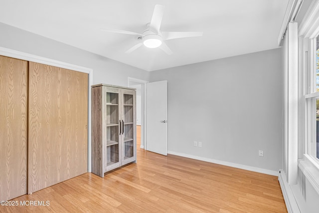 unfurnished bedroom featuring a baseboard radiator, a closet, ceiling fan, light wood-style flooring, and baseboards