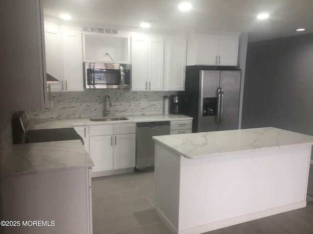 kitchen with white cabinets, a sink, light stone countertops, tasteful backsplash, and appliances with stainless steel finishes