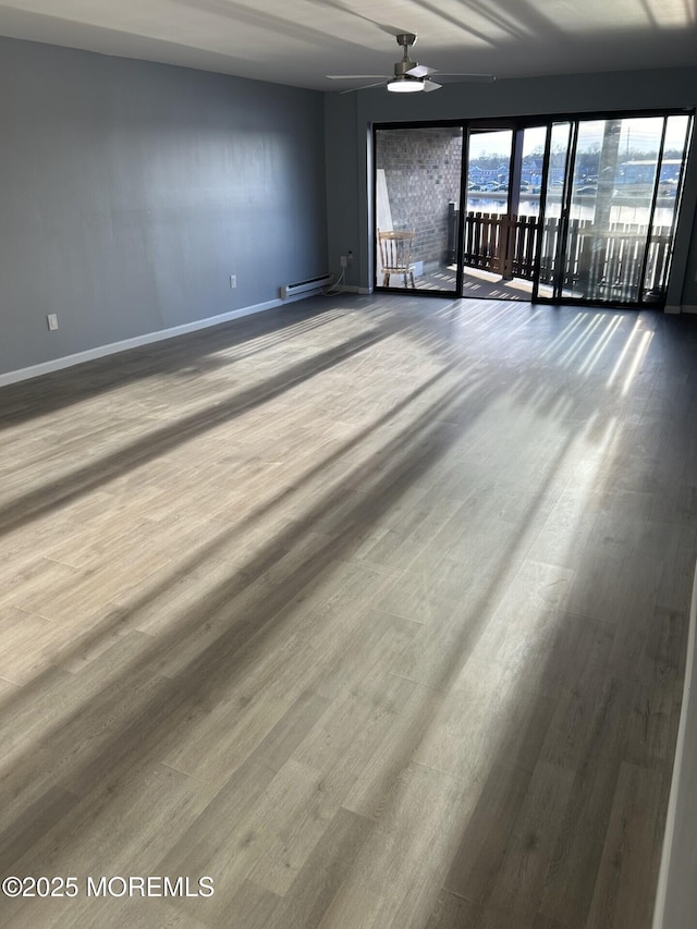 empty room with a baseboard heating unit, ceiling fan, baseboards, and wood finished floors