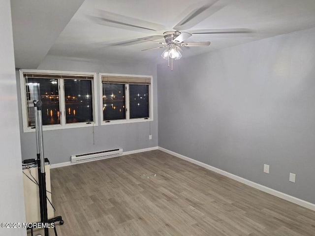 empty room featuring a baseboard heating unit, wood finished floors, baseboards, and ceiling fan