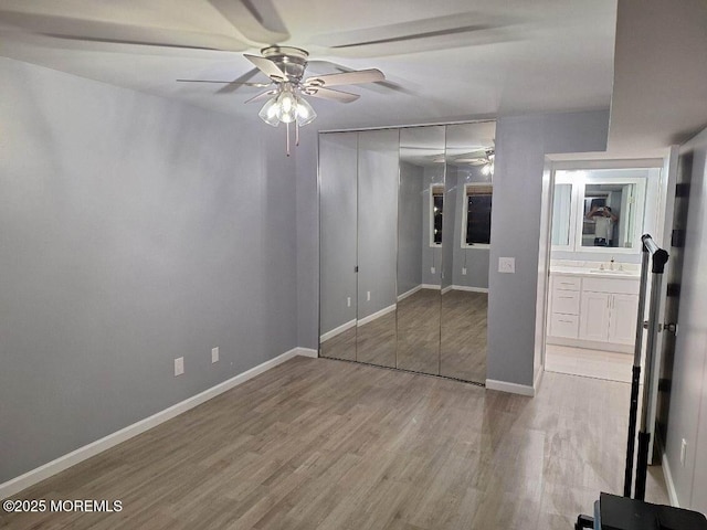unfurnished bedroom featuring a sink, wood finished floors, a closet, ceiling fan, and baseboards