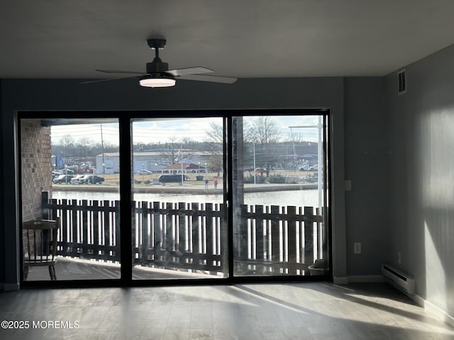 interior space featuring wood finished floors, visible vents, a ceiling fan, baseboards, and a baseboard radiator