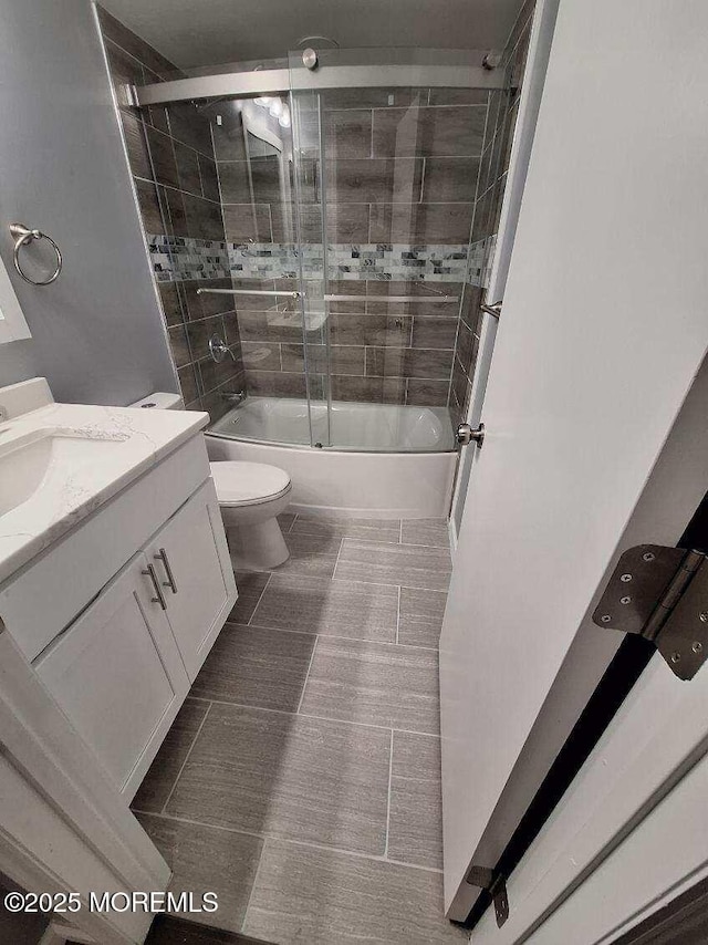 bathroom with tile patterned floors, vanity, shower / bath combination with glass door, and toilet