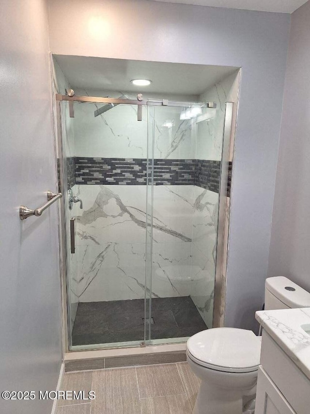bathroom with a marble finish shower, vanity, and toilet