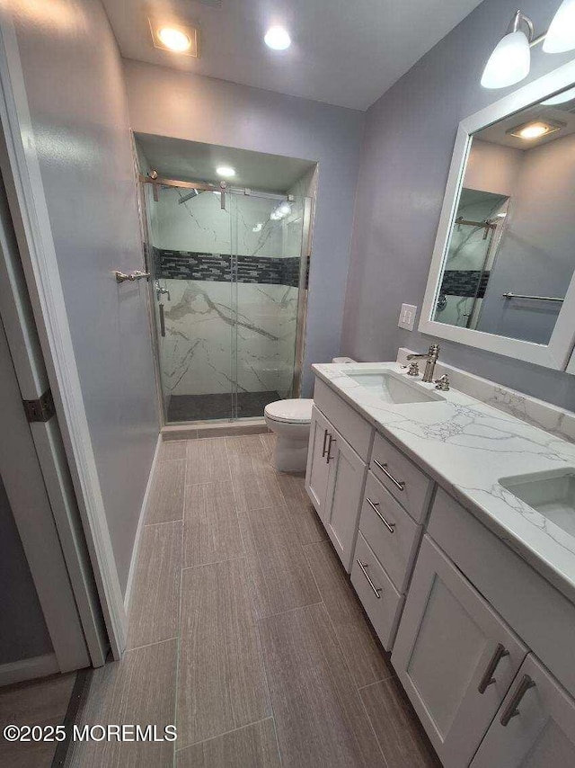 full bath featuring a marble finish shower, a sink, double vanity, and toilet