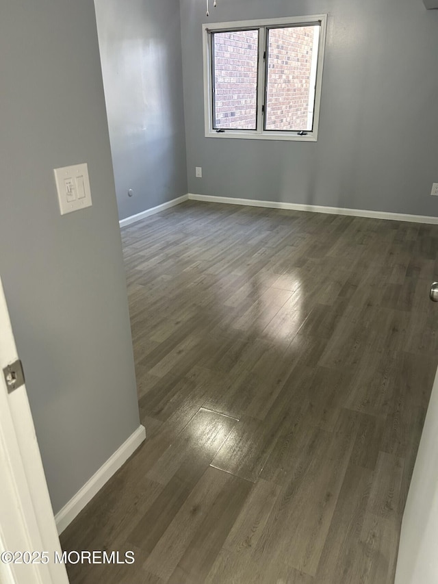 spare room with baseboards and dark wood-style floors
