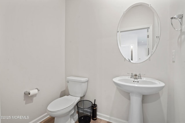 half bathroom featuring baseboards, toilet, and wood finished floors