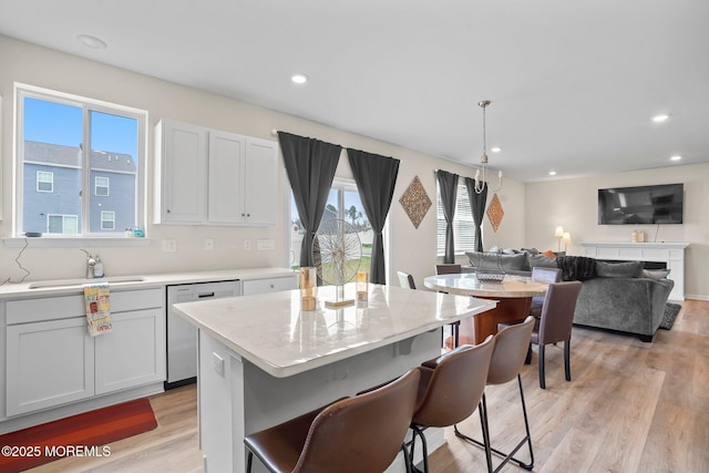 kitchen featuring light wood-style flooring, a sink, recessed lighting, dishwasher, and a breakfast bar