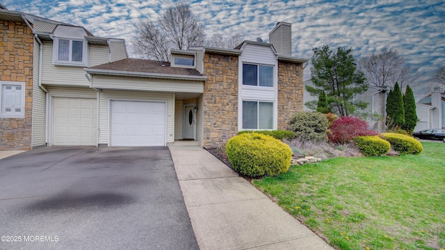 view of front of home featuring a front yard, stone siding, an attached garage, a chimney, and driveway