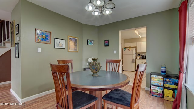 dining area featuring a chandelier, light wood finished floors, baseboards, and stairway