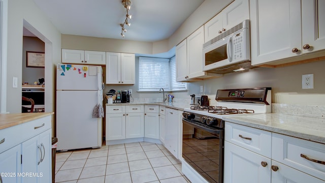 kitchen with light tile patterned floors, a sink, white appliances, white cabinetry, and light stone countertops