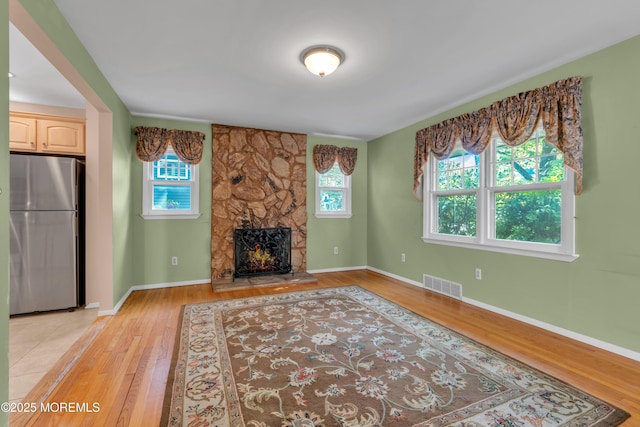 unfurnished living room featuring visible vents, baseboards, a stone fireplace, and light wood-type flooring