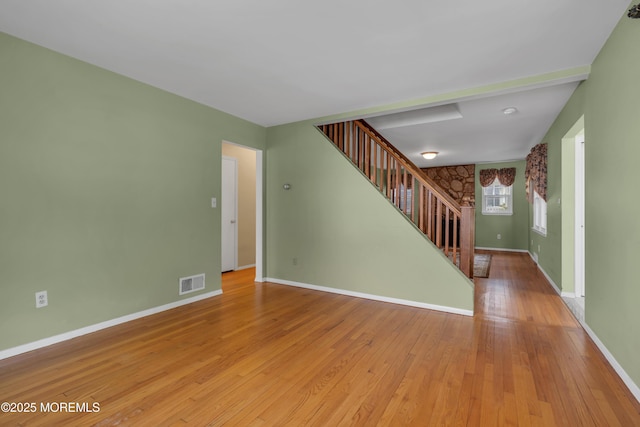 unfurnished living room with visible vents, light wood-style flooring, baseboards, and stairway