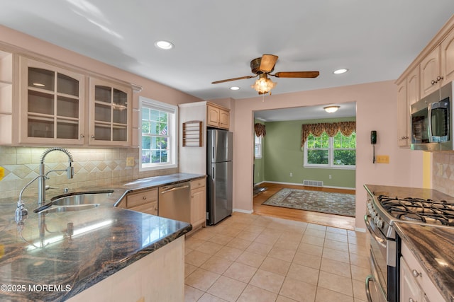 kitchen featuring a ceiling fan, tasteful backsplash, a sink, glass insert cabinets, and stainless steel appliances