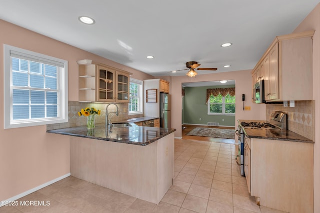 kitchen featuring light brown cabinetry, appliances with stainless steel finishes, a sink, and dark stone countertops