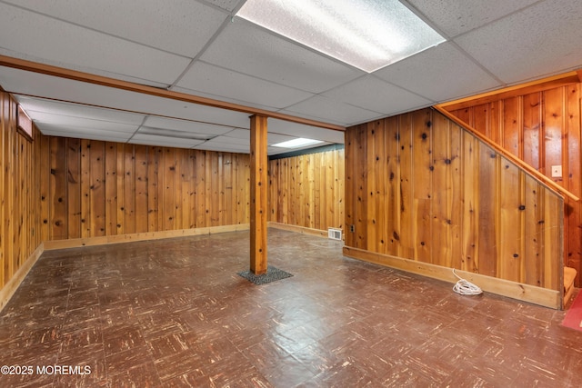 finished below grade area featuring wooden walls, tile patterned floors, visible vents, and a paneled ceiling
