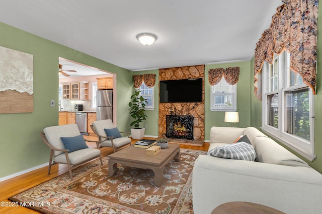 living area featuring baseboards, ceiling fan, light wood-style flooring, and a fireplace