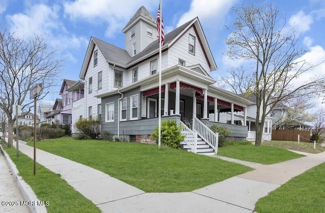 victorian house featuring a front yard, fence, and covered porch