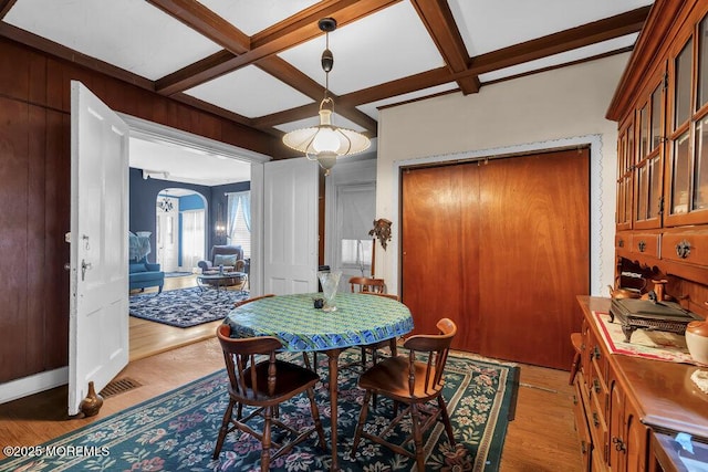 dining area featuring arched walkways, wood finished floors, beam ceiling, and coffered ceiling