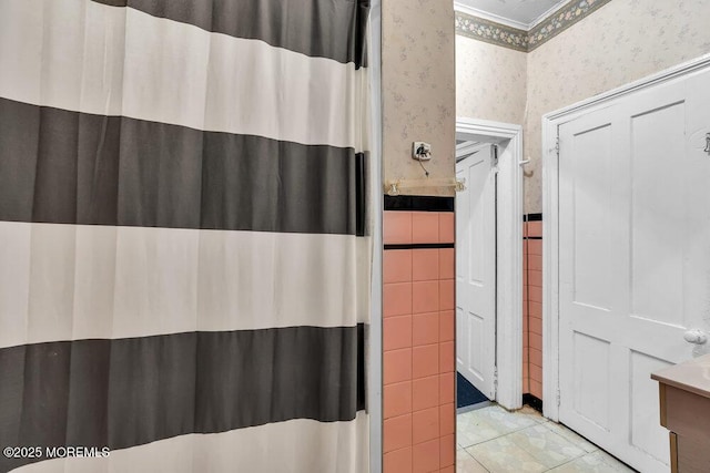 bathroom with wallpapered walls, a shower with curtain, wainscoting, and tile walls